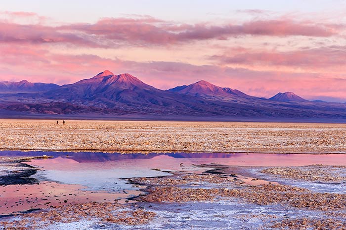 Puesta de sol en el Salar de Atacama, Atacama, Chile, con pequeñas lagunas en primer plano y montañas al fondo