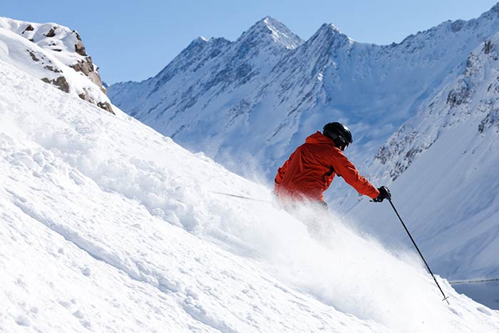 Skier in orange jacket and black helmet on the fresh snow covered slopes of Portillo mountain resort